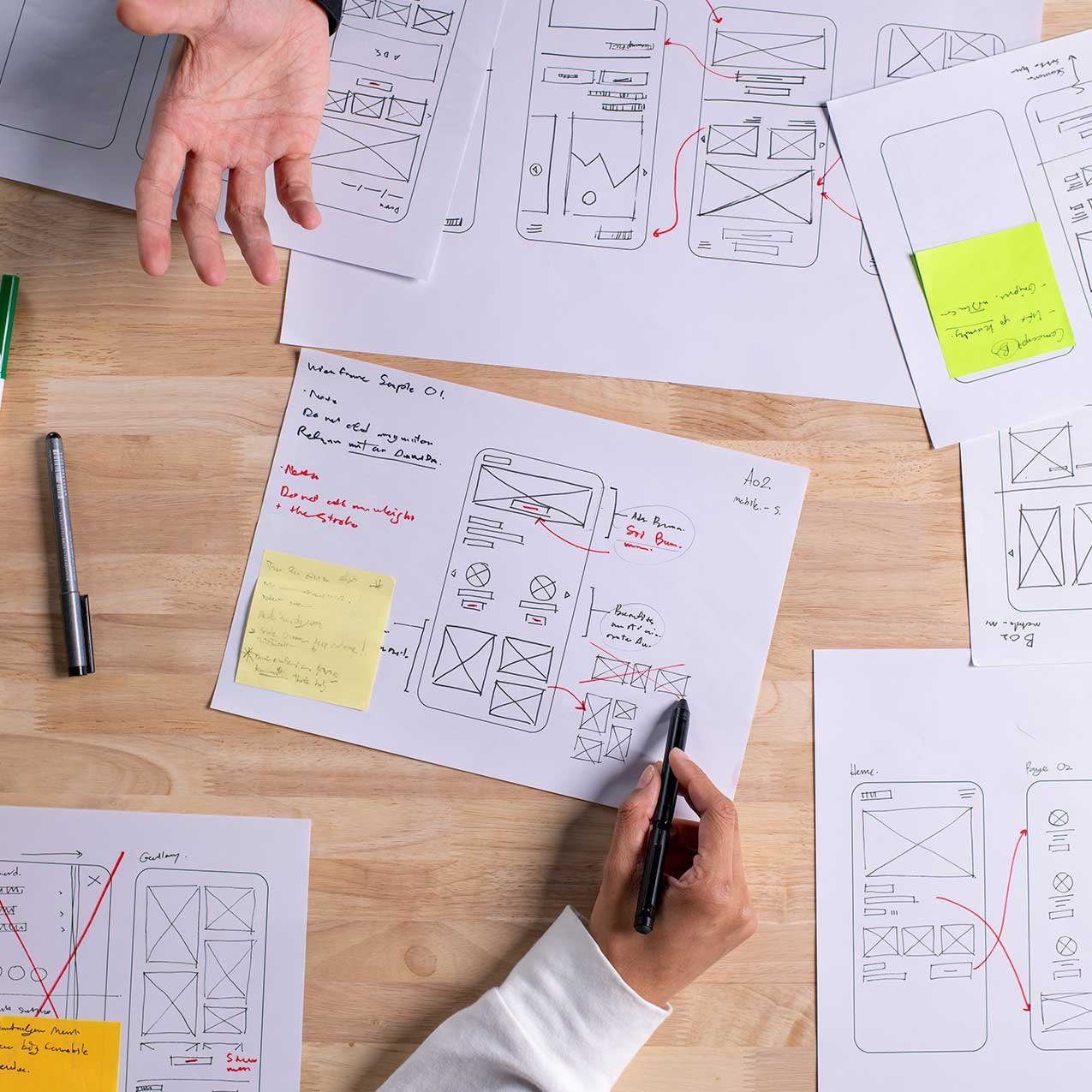 User interface wireframes and sketches being reviewed and edited on a wooden table